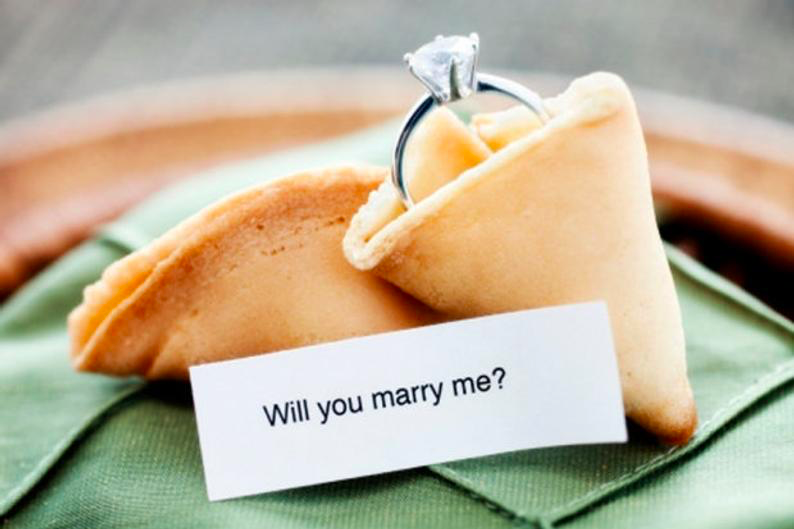 proposing fortune cookie on a green napkin with an engagement ring and will you marry me on the note