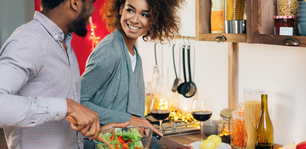 Cooking lunch together. Smiling african-american couple preparing salad at kitchen, copy space